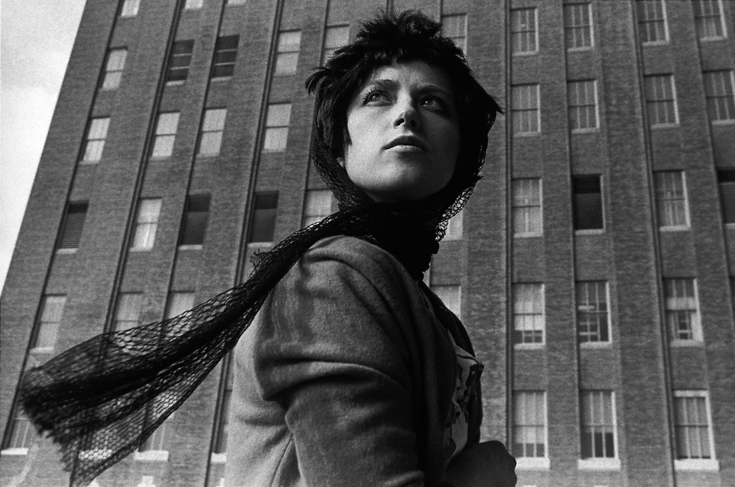 cindy sherman with a head scarf in front of a multilevel story building