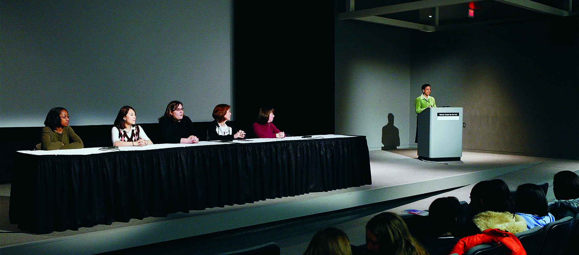 five panelists at long table on stage and one speaker at podium