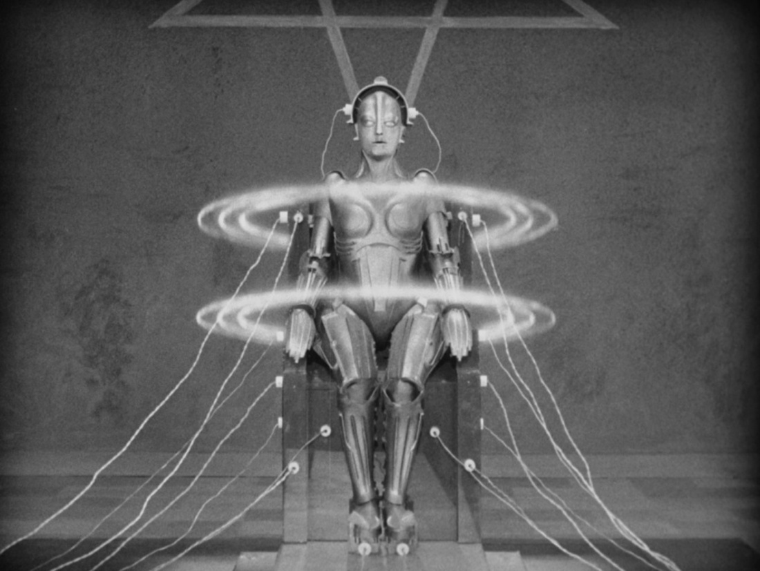 A black and white image of a robot with a female form. It sits in a chair with wired electrodes attached to it. Volts of electricity encircle its body and 
