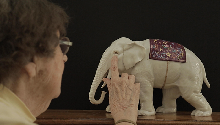 An older woman is touching the eye of a white elephant figurine.