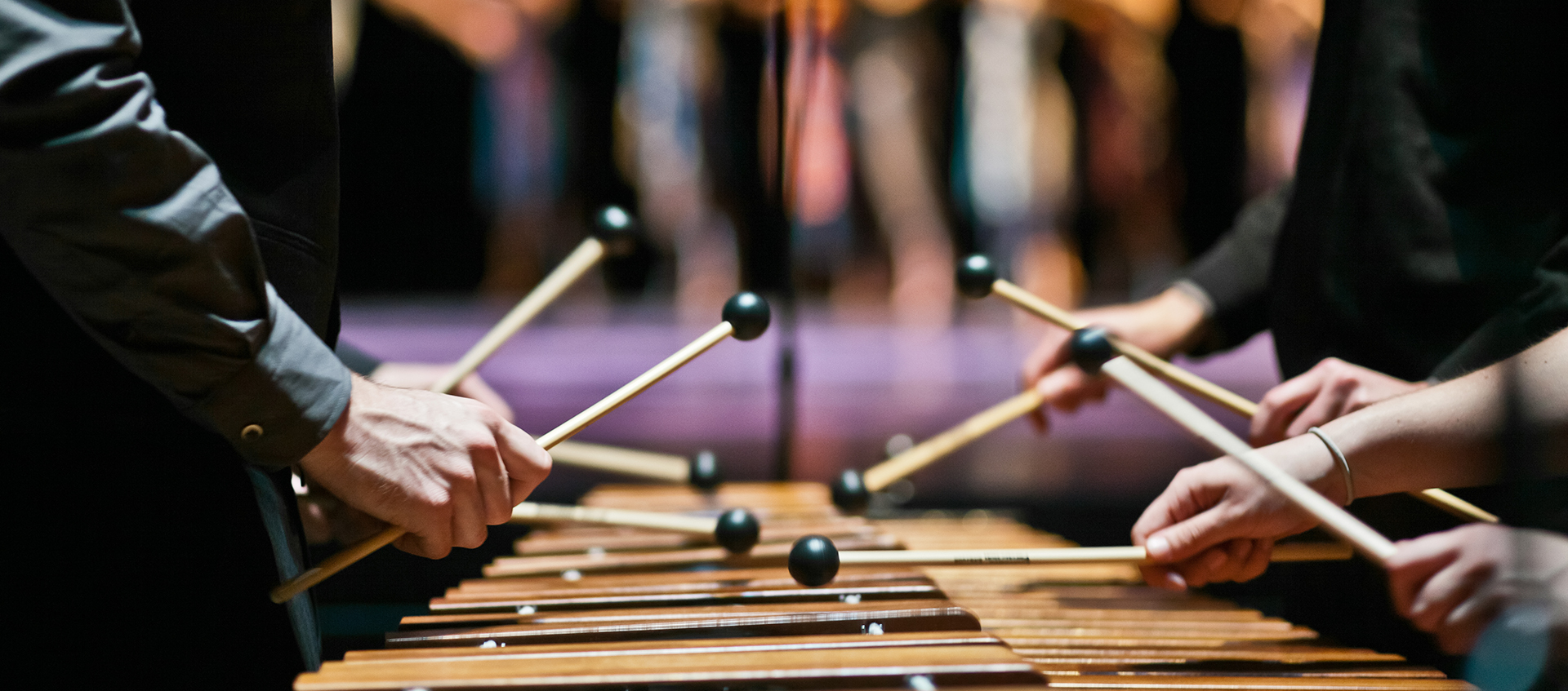 A group of percussionists play a marimba, only their hands and arms are visible in the frame.