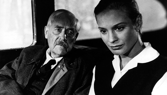 Black and white photo of an older male actor and younger female actress sitting in a car.
