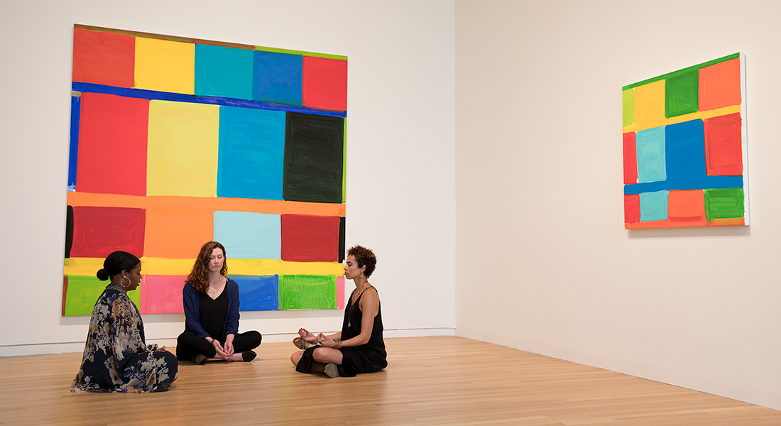 three women in a yoga pose in front of two colorful art installations
