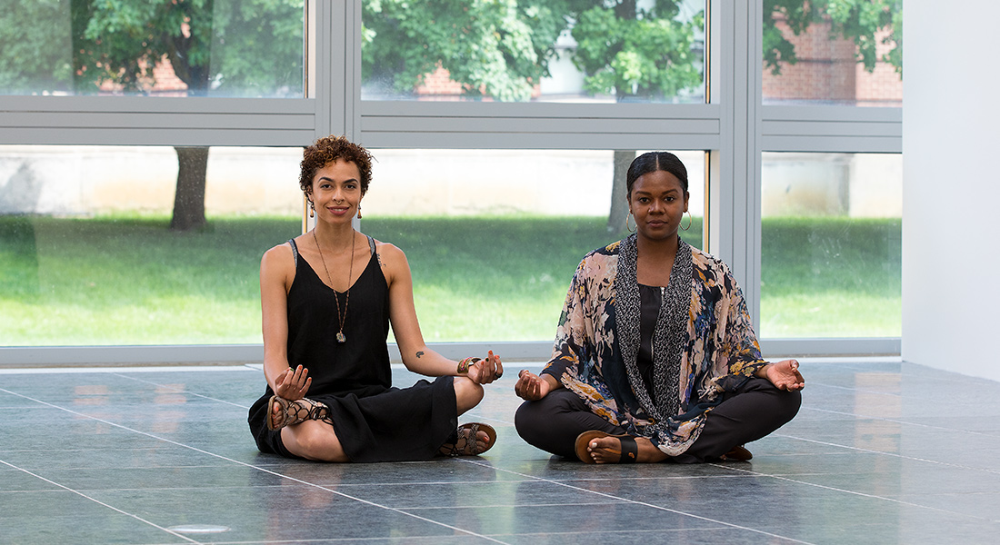 two women in a yoga pose against a large glass wall in the Wexner Center gallery space