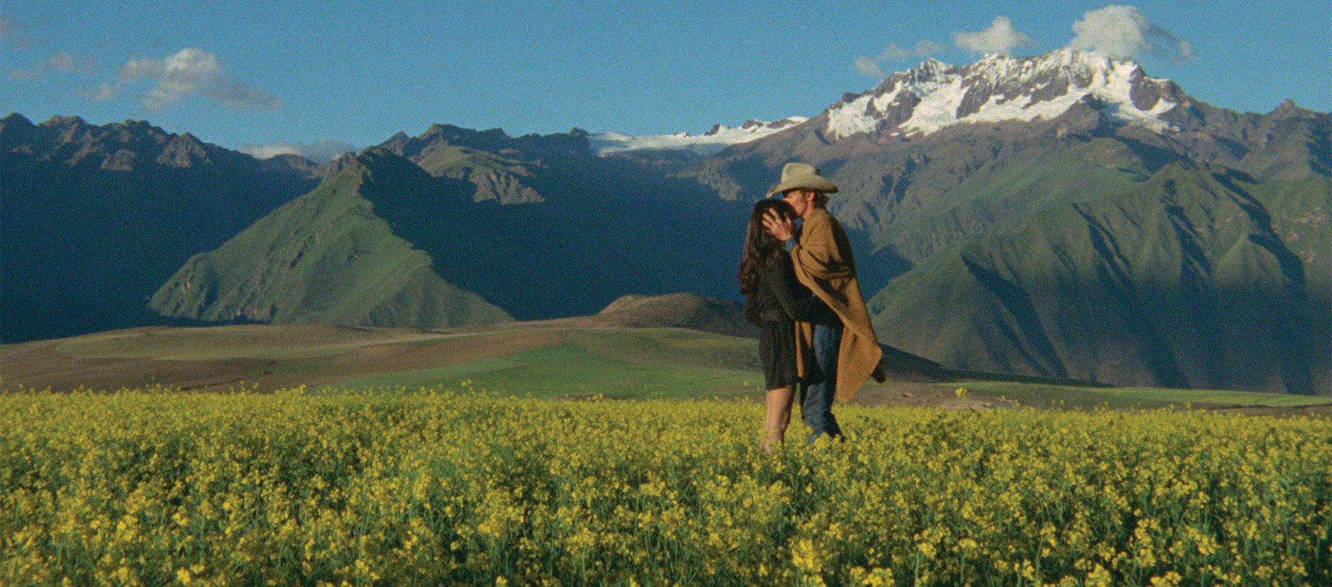 Two people standing in the middle of a prairie with snow capped mountains in the background