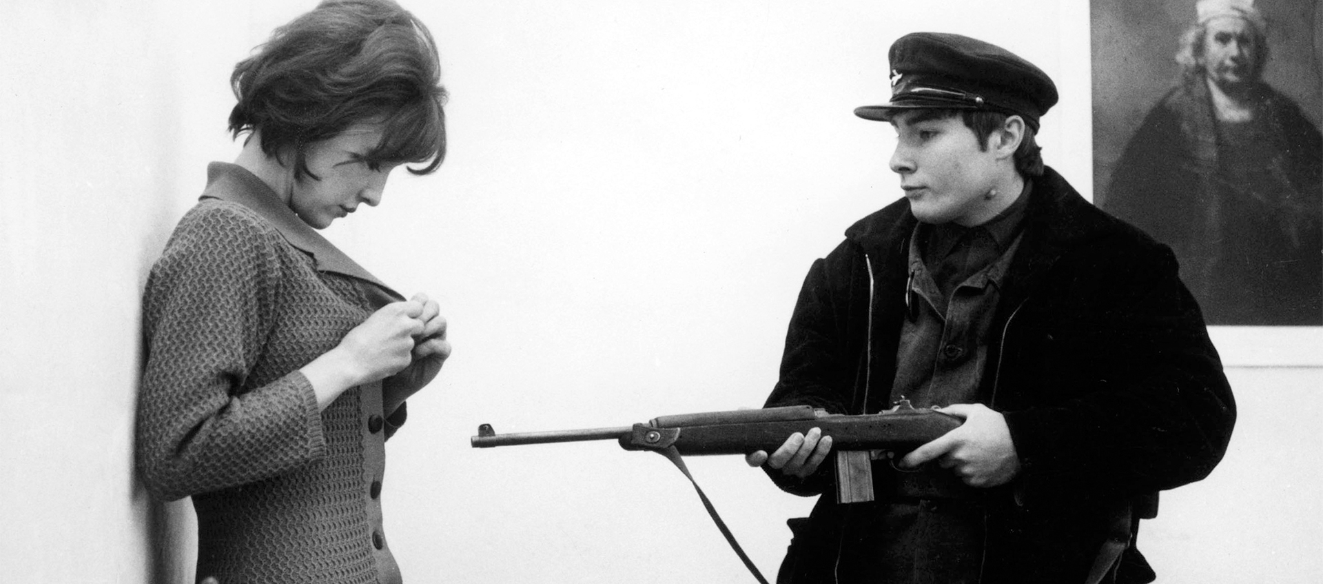 A man holds a rifle at a women in a black and white movie still