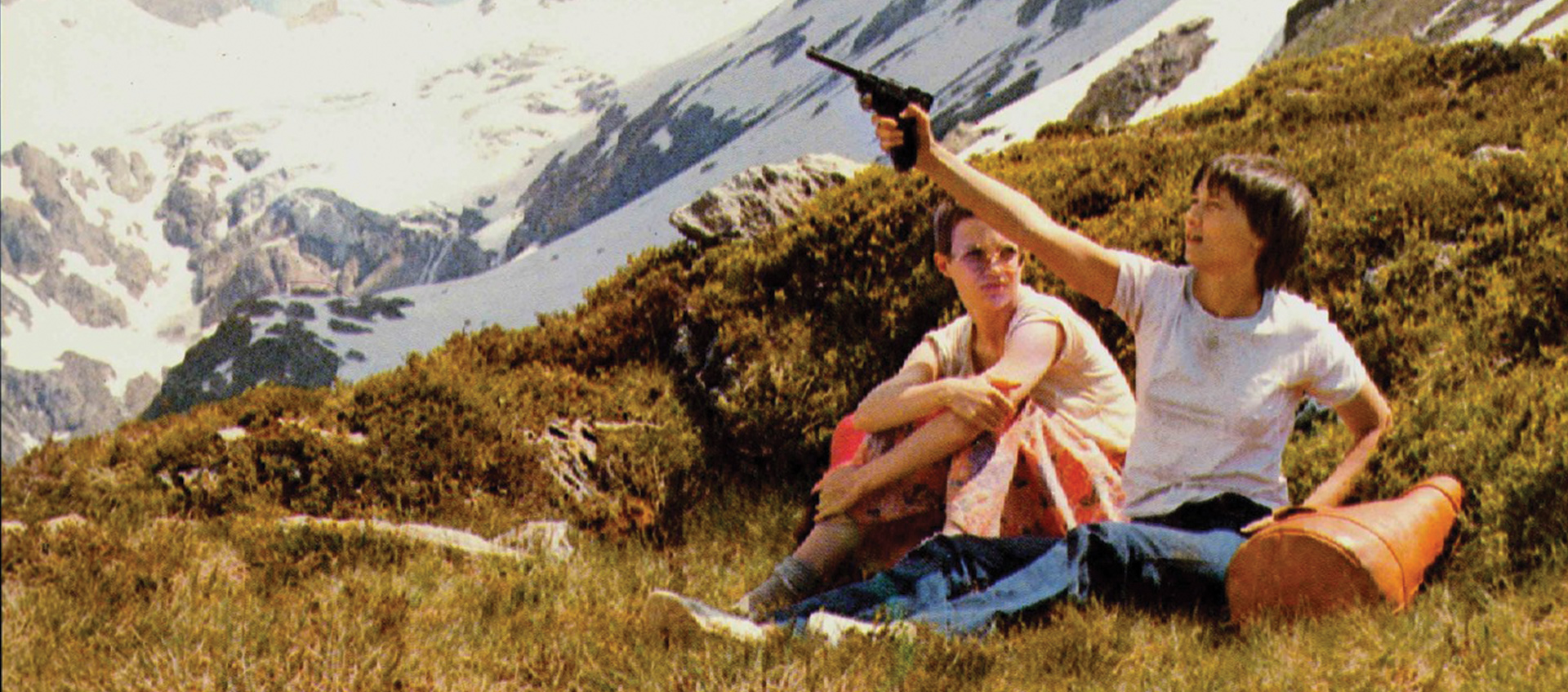 Two woman sit on mountainside, one holds a gun