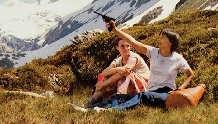 Two woman sit on mountainside, one holds a gun
