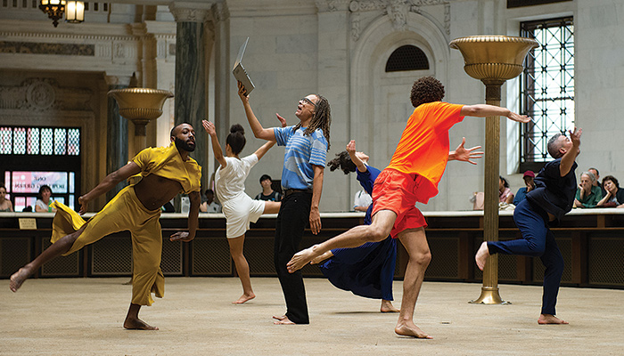 Five dancers encircle a sixth performer holding a laptop