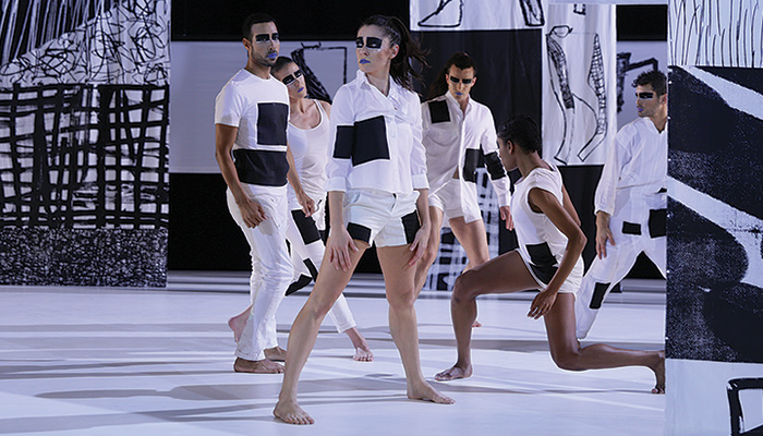 Dancers dressed in black and white stand on a black and white stage