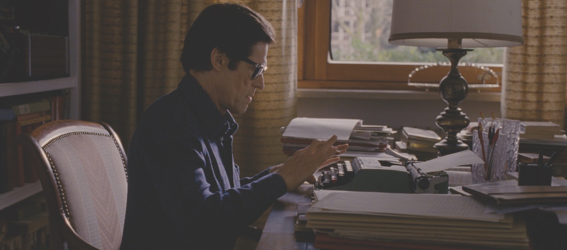 Willem Dafoe as filmmaker Pier Paolo Pasolini sits at a desk and types in a still from Abel Ferrar's biopic Pasolini, courtesy of Kino Lorber Films 