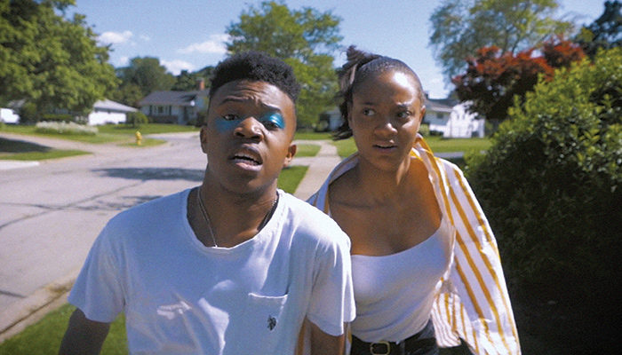 Head & shoulders images of a young black man and woman running down a suburban street in a scene from the short film COVE (Illegal Alien) by Ryan Wise