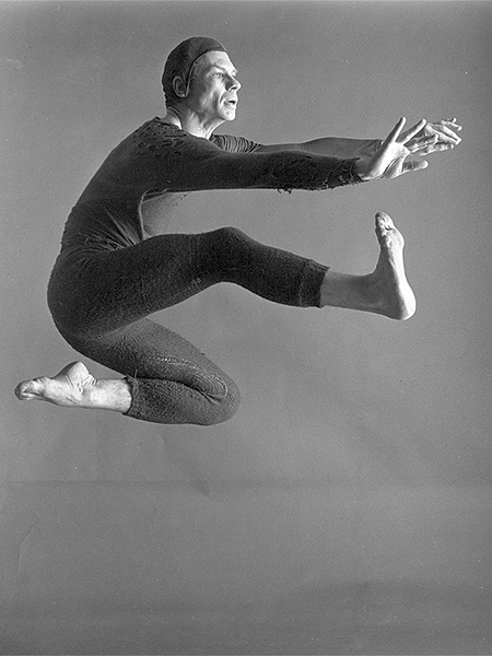 Black and white portrait of dancer-choreographer Merce Cunningham, caught mid-jump. 
