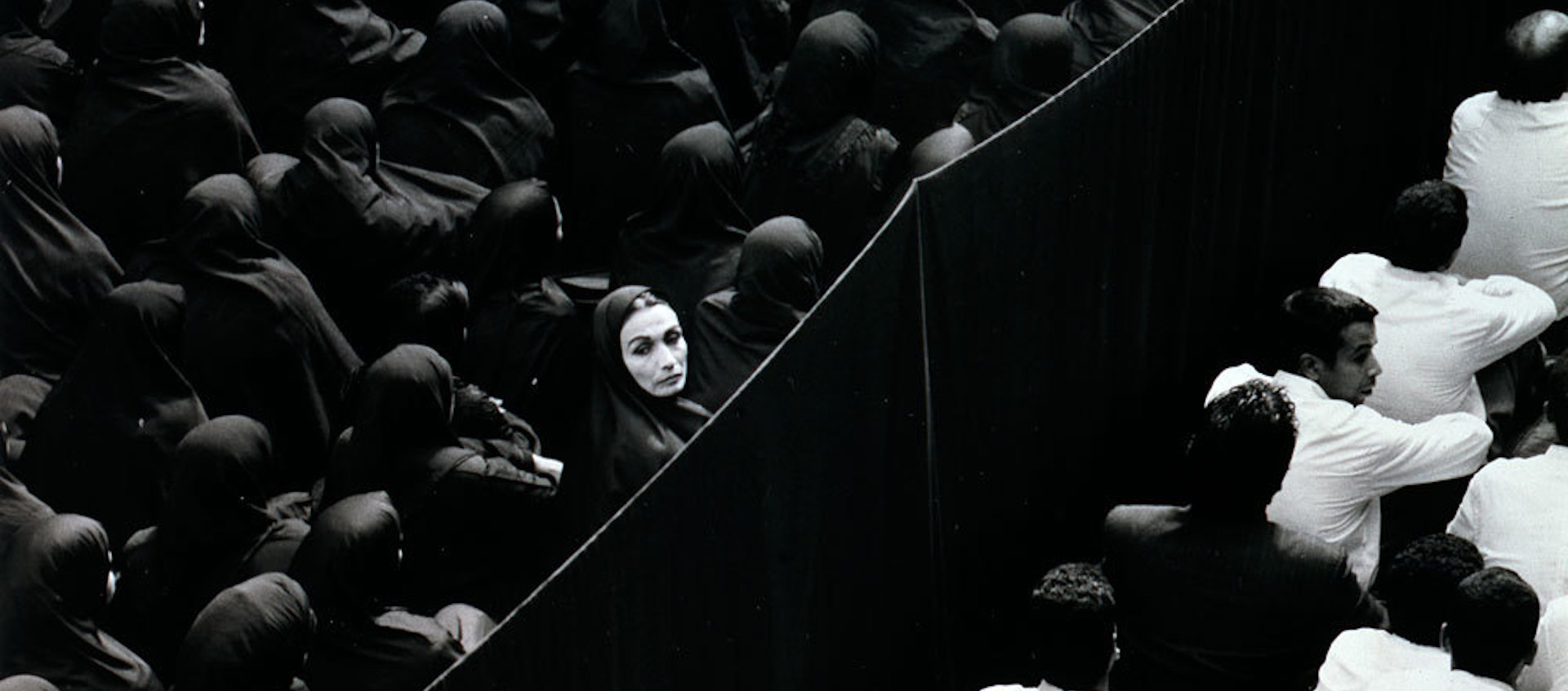 A black and white dual projection image of gender-segregated crowds from the Shirin Neshat video installation Fervor