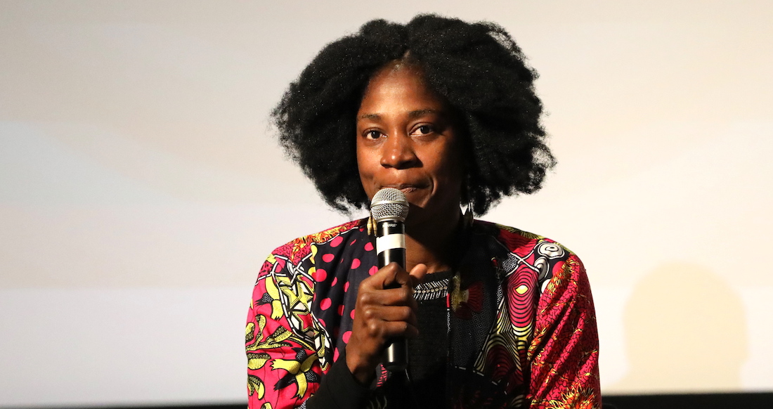 Cameroonian filmmaker Rosine Mbakam speaks into a microphone while sitting on the stage of the Wexner Center for the Arts in October 2019