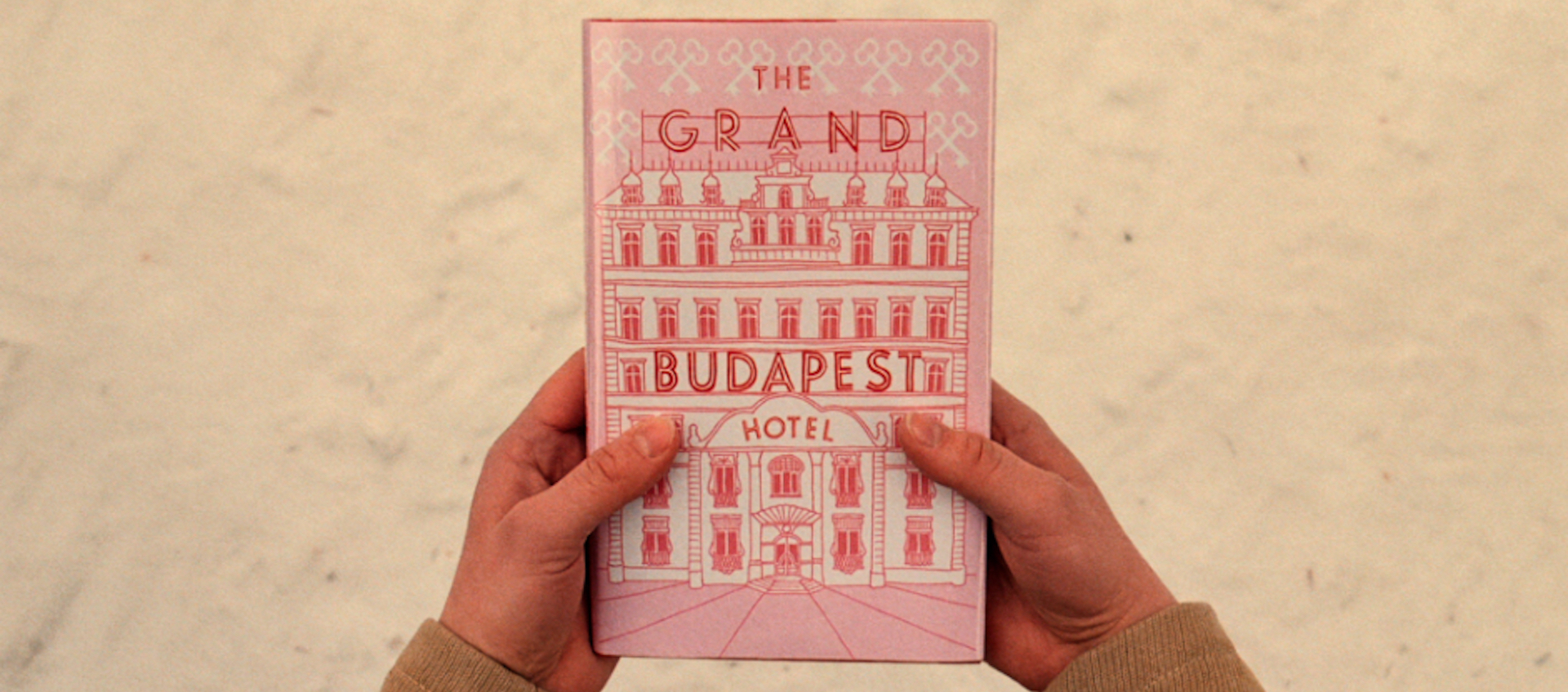 A picture of hands holding the fictional book The Grand Budapest Hotel, designed by Annie Atkins