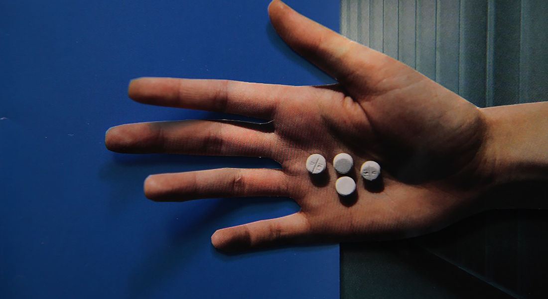 In this color collage, a still from the film, a hand holds four white pills in its palm against a blue background.