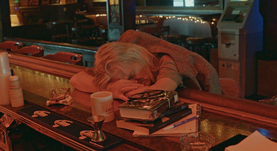 A man with white hair appears to nap on a bar in a scene from Bloody Nose, Empty Pockets