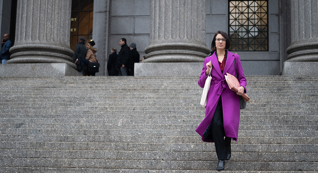 A dark haired woman in glasses and a purple coat walks down courthouse steps in the documentary The Fight