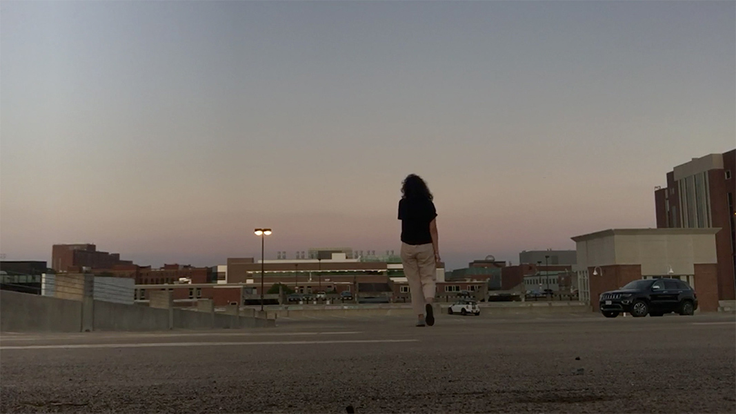 A person stands on a rooftop looking at a dusk or dawn sky.