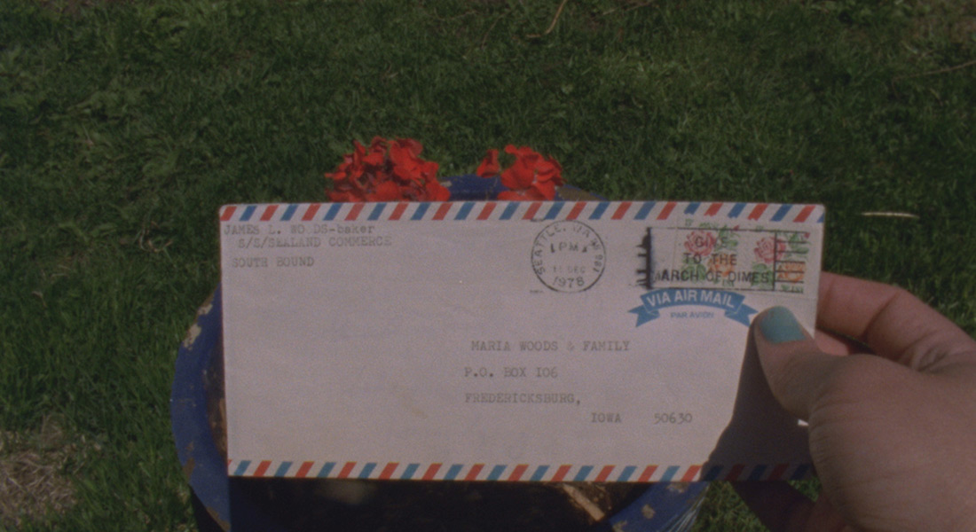 A close up of a hand holding an air mail envelope addressed to Maria Woods & Family