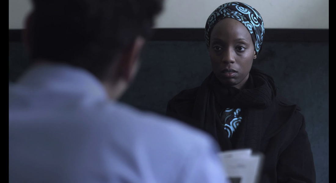 A women in a headscarf and worried expression looks at a interlocutor with his back to camera