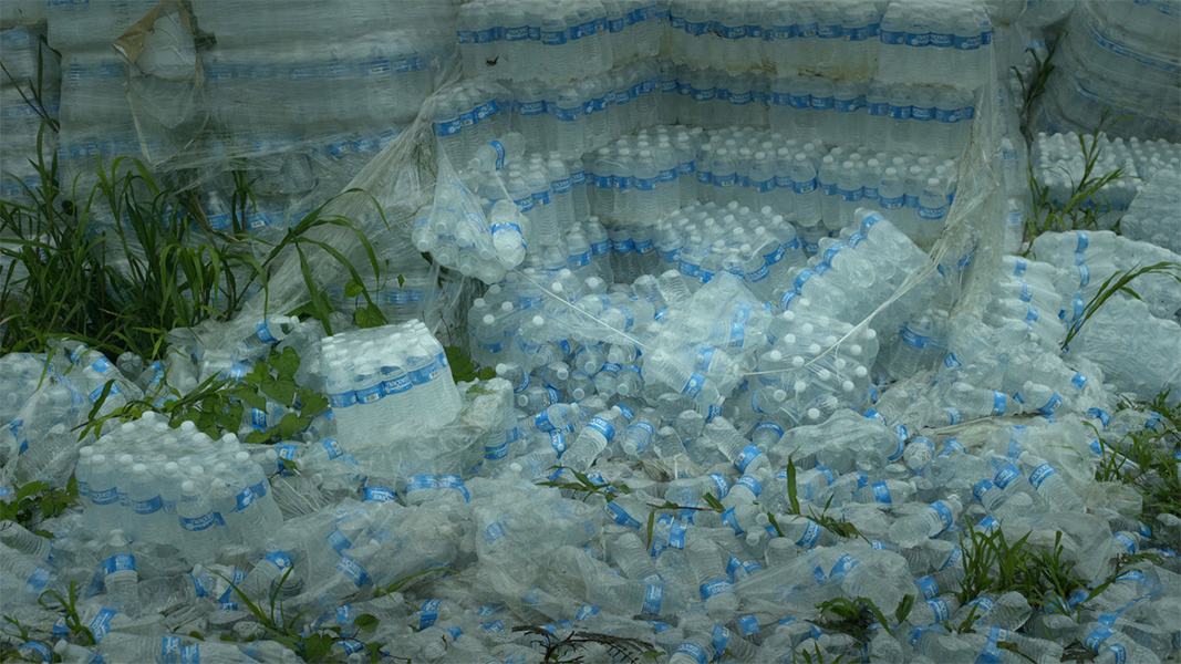 Hundreds of cases of water bottles are strewn on the ground and stacked in rows.