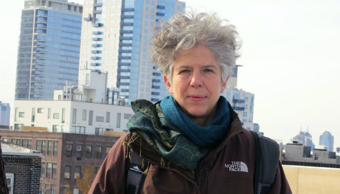Filmmaker Su Friedrich stands in a winter jacket on a Brooklyn rooftop with part of the skyline in the background