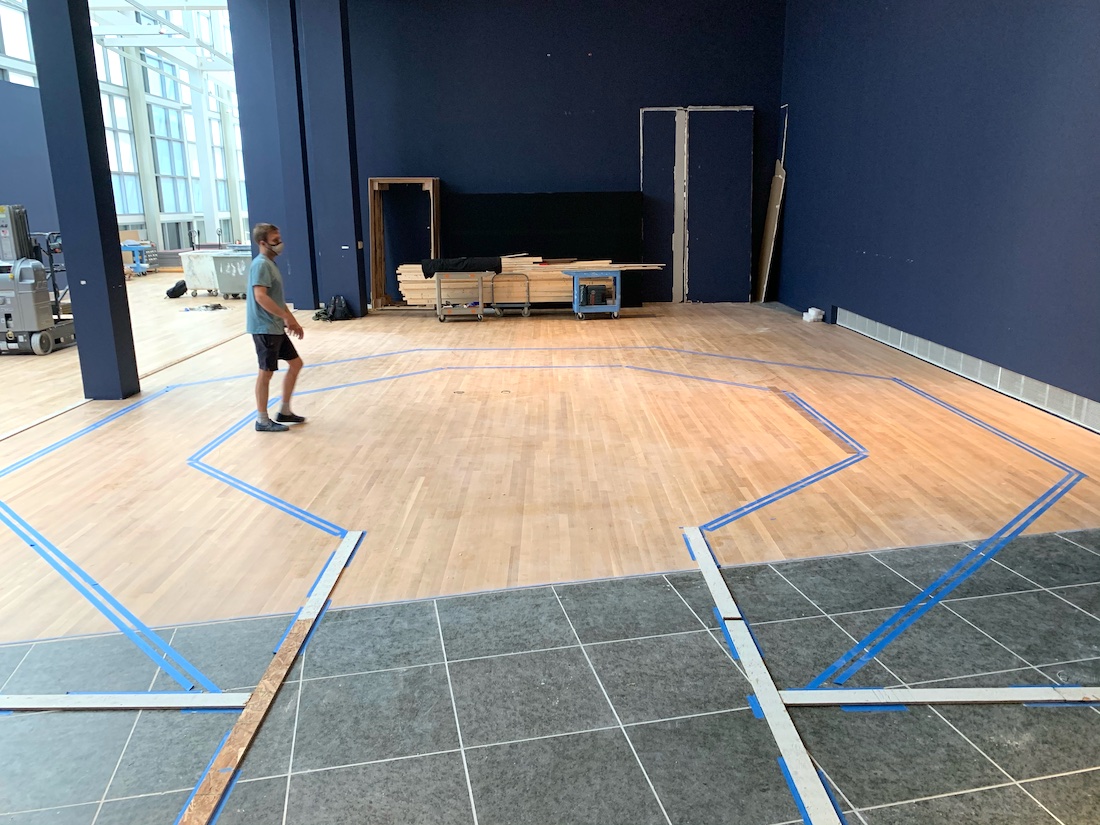 A preparator at the Wexner Center for the Arts stands in one of the gallery spaces, surrounded by tape lines on the floor that mark out the eventual layout of the installation Taryn Simon: Assembled Audience