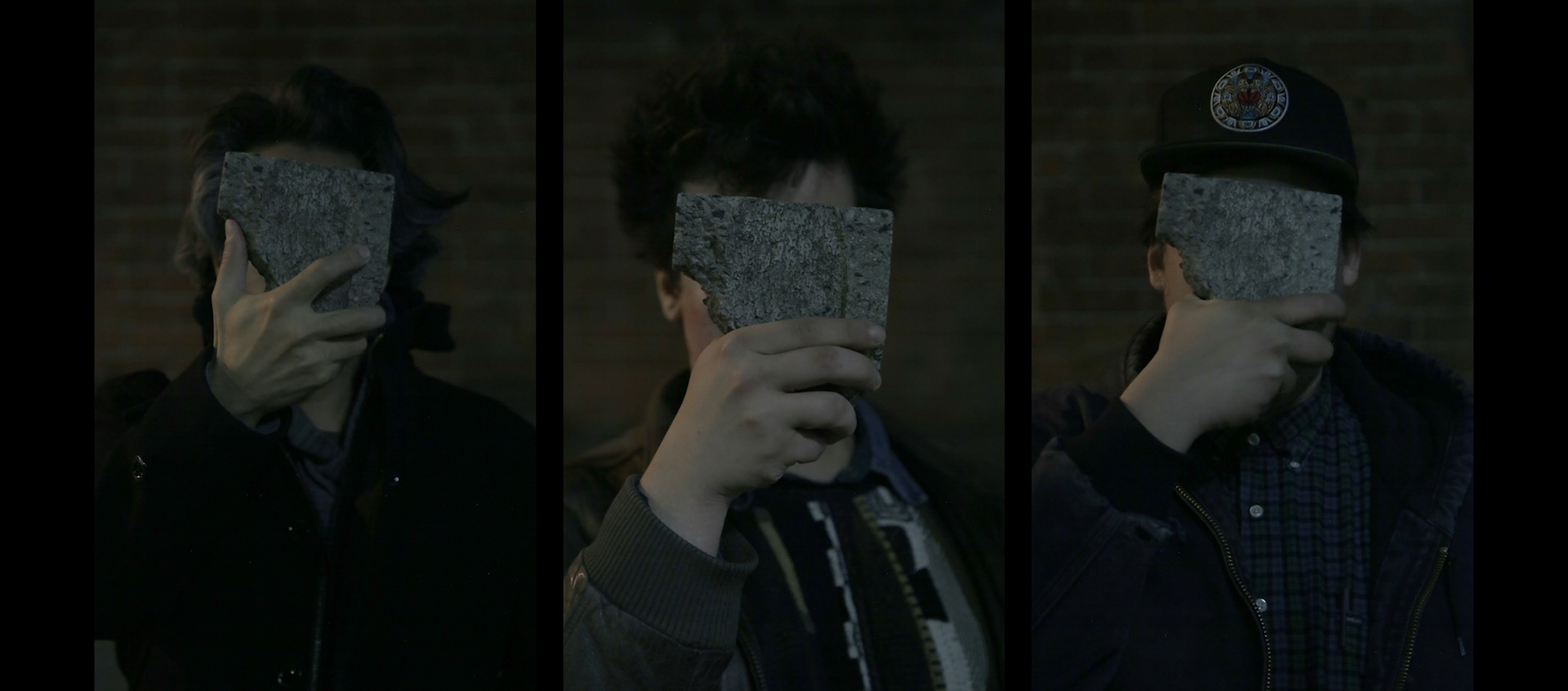 A photo of three members of New Red Order, they are all covering their faces with a piece of stone