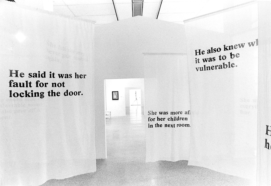 A black-and-white image of an artwork framing a gallery entranceway that consists of phrases in roman type displayed on blank fabric curtains hanging from the ceiling. The visible phrases read “He said it was her fault for not locking the door,” “She was more afraid for her children in the next room,” and “He also knew what it was to be vulnerable.”