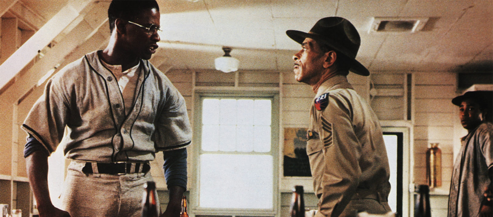 Denzel Washington in jeans and gray shirt, wearing eyeglasses stands in front of a military officer and is telling at him
