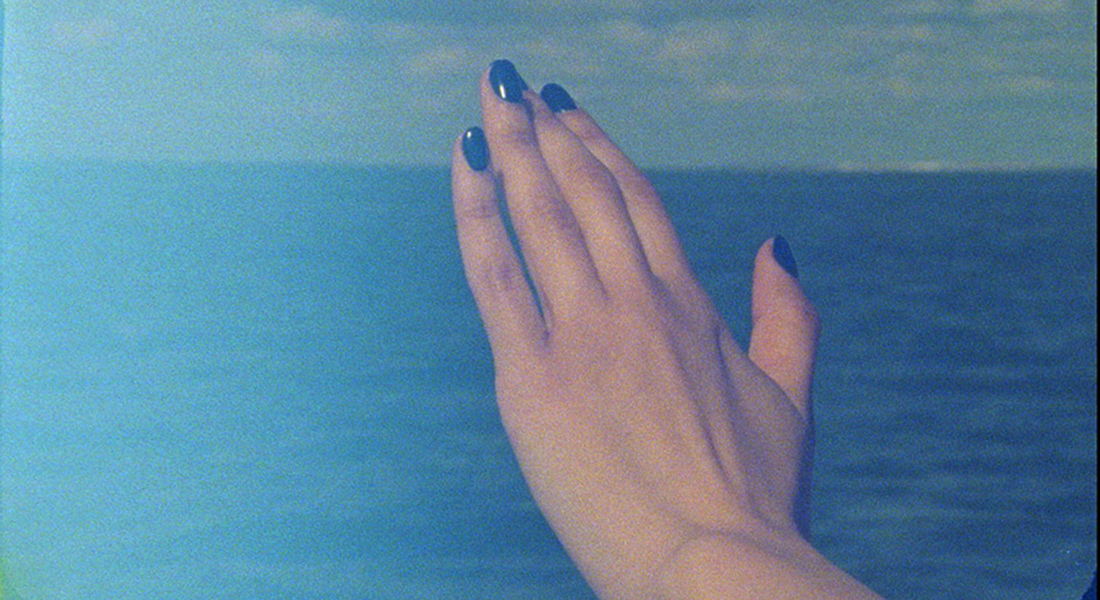 A pale hand with its palm down and purple fingernail polish is overlaid an image of a body of water