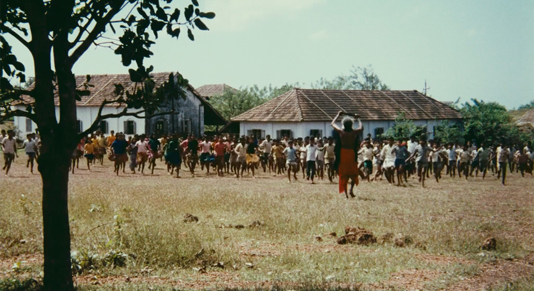 A large group of people stand outdoors in a village