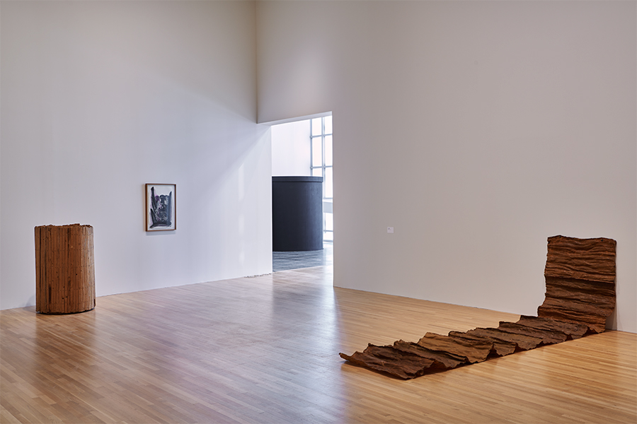 A photograph of Jackie Winsor's wood sculpture Cylinder Lattice (1971) and Eva Hesse's latex sculpture Area (1968) installed in the exhibition To Begin, Again: A Prehistory of the Wex, 1968–89.