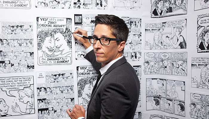 Alison Bechdel standing in front of a wall of comic panels