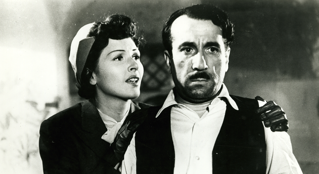 Black-and-white still from Variety Lights featuring Lily (Carla Del Poggio) and Checco (Peppino De Filippo). Lily (left) has her hands, which are covered in black gloves, on Checco’s shoulders as he looks straight ahead.
