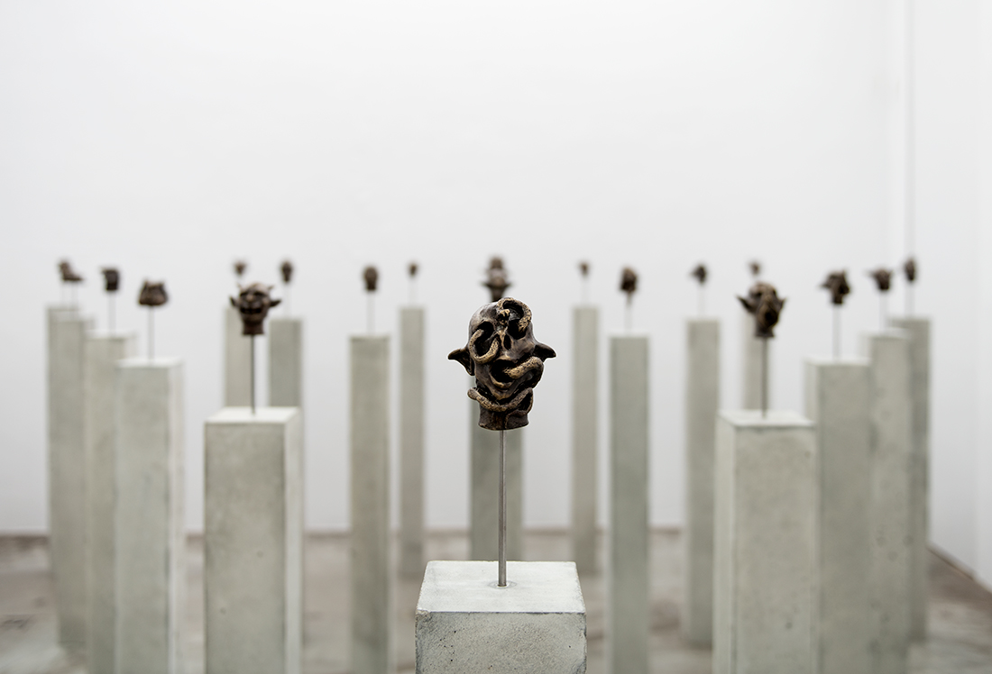 A group of small bronze sculptures on concrete pedestals in a white gallery space