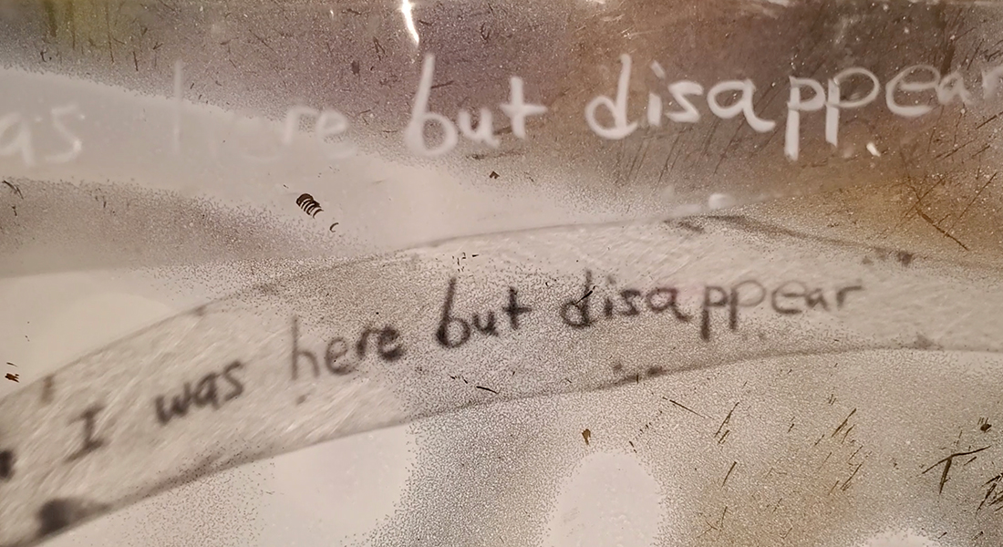 The words “I was here but disappear” written twice against a grainy, scratched background of brown shades. 