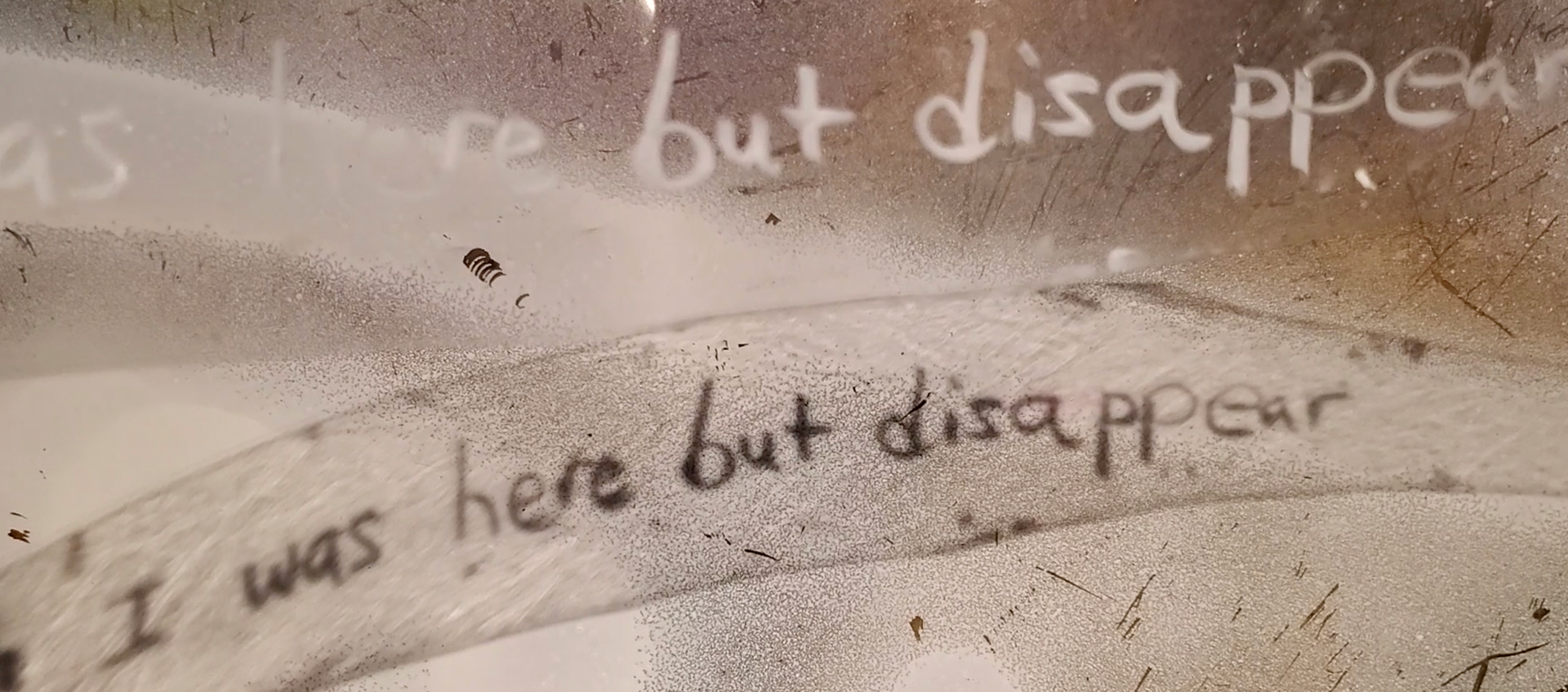 The words “I was here but disappear” written twice against a grainy, scratched background of brown shades.