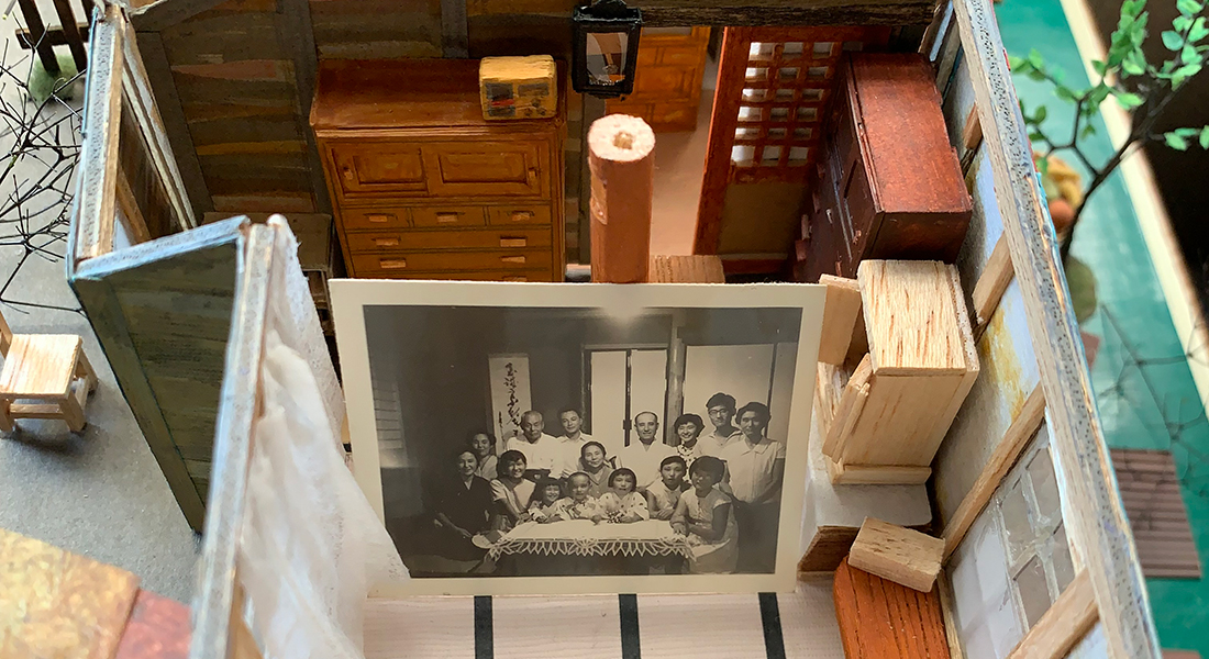 A black-and-white photo of a large group of people is nestled within a diorama of a home