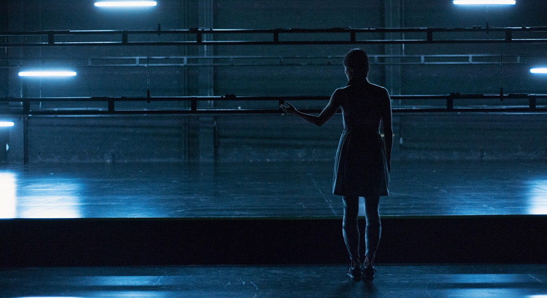 An image of a solitary dancer on a stage lit in blue from Radouan Mriziga's movement work 7